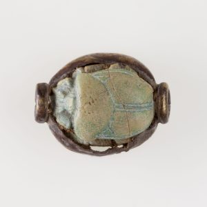 Ancient Egyptian blue glazed steatite scarab decorated with papyrus plants and winged beetles symbolizing rebirth and protection.