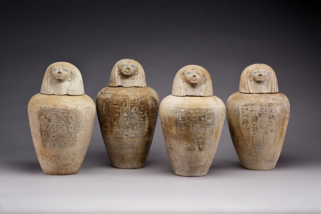 Four ancient Egyptian canopic jars of Ruiu with human-headed lids and incised hieroglyphic inscriptions.